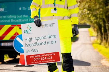 Worker holding a sign with "High speed broadband is on the way" wrote on it