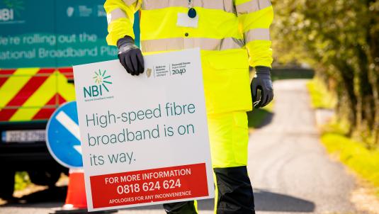 Worker holding a sign with "High speed broadband is on the way" wrote on it